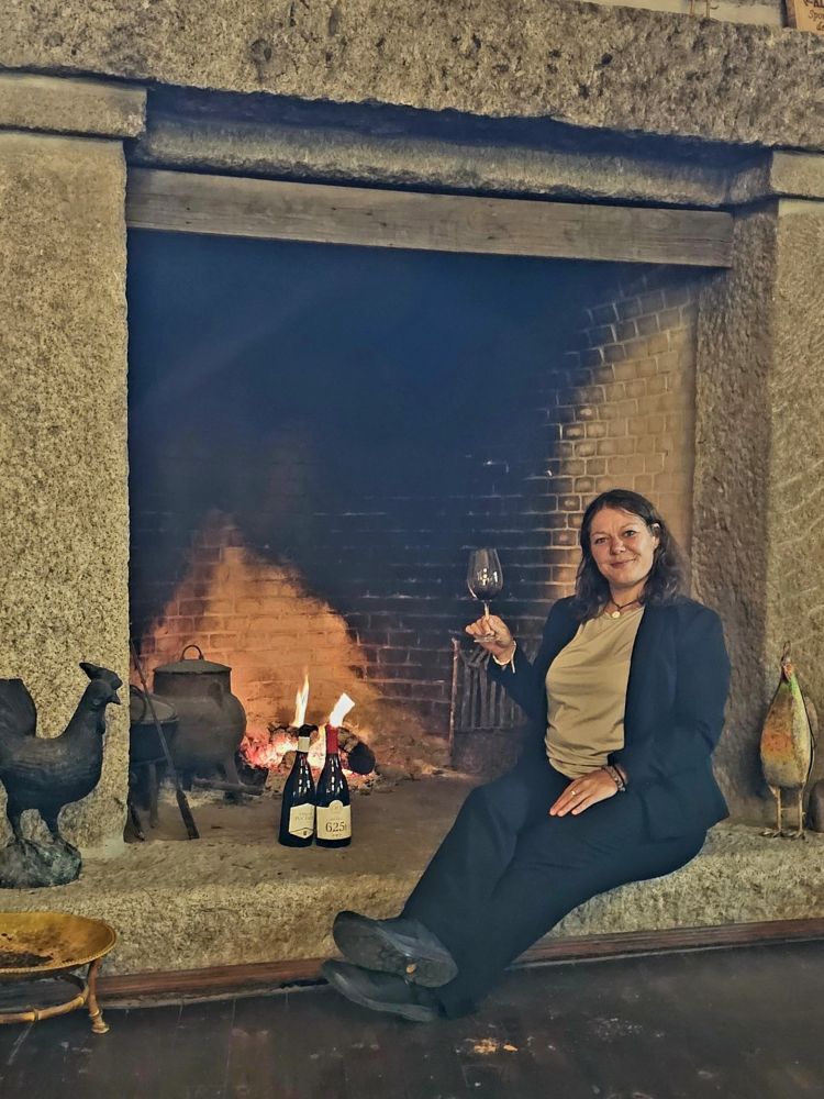 Weinsommelière Lisa in Portugal mit einem Glas Rotwein an einem Kamin.